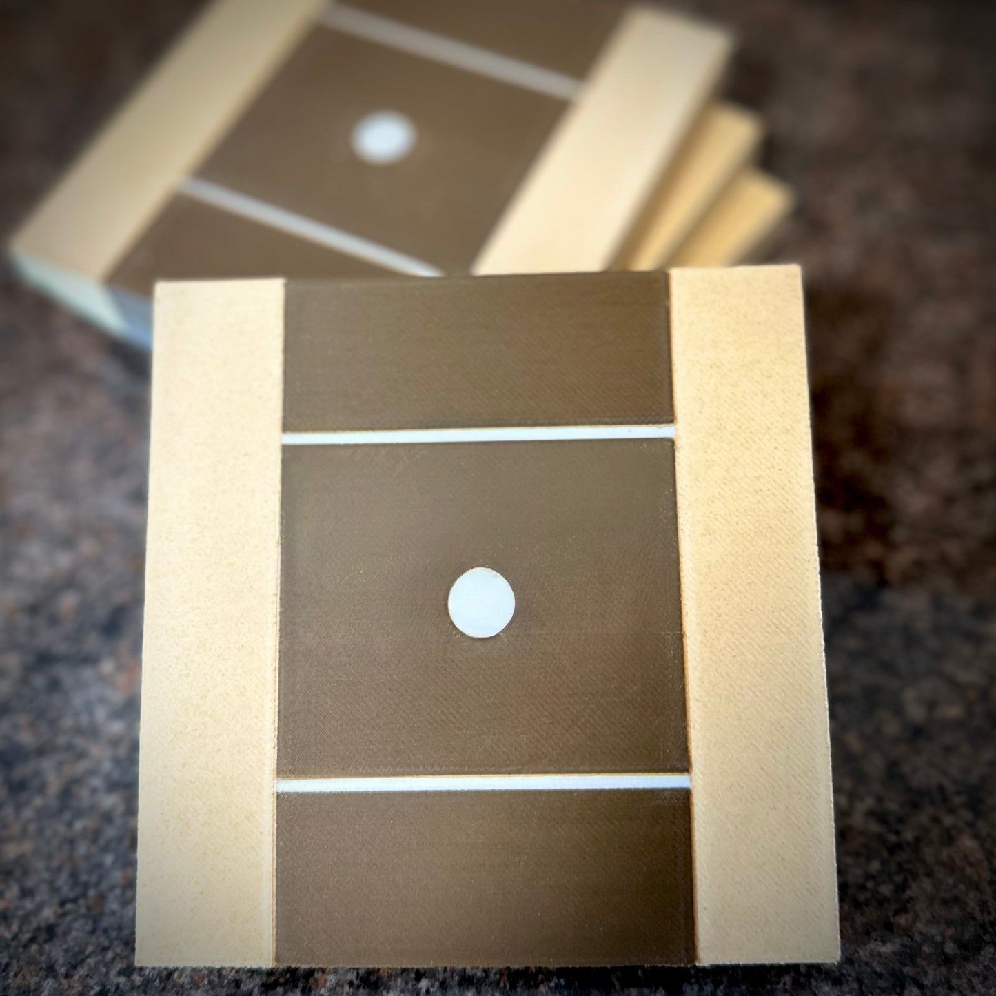 4 square guitar neck Coasters 4" 100mm square in size with light maple colour edges and walnut colour in the middle to signify the guitar fretboard with Stratocaster dot inlay. One coaster in the foreground with 4 behind using bokeh effect.